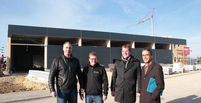 Auf dem Bild sieht man den Neubau der Produktionshalle im Rohbau und davor 4 Personen stehen: Von links: Gesellschafter Jürgen Silge, Geschäftsführer Oliver Schmid, Ingbert Binz von Holzbau Binz und Oberbürgermeister Karl Hilsenbek.